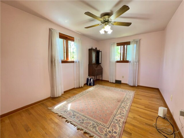 empty room with a ceiling fan, baseboards, a wealth of natural light, and light wood finished floors