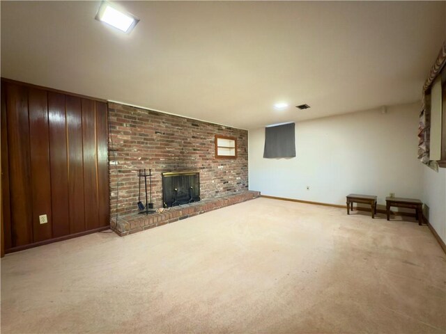 unfurnished living room featuring visible vents, wood walls, a brick fireplace, baseboards, and carpet flooring