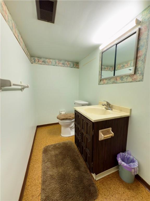 half bath featuring vanity, baseboards, toilet, and visible vents