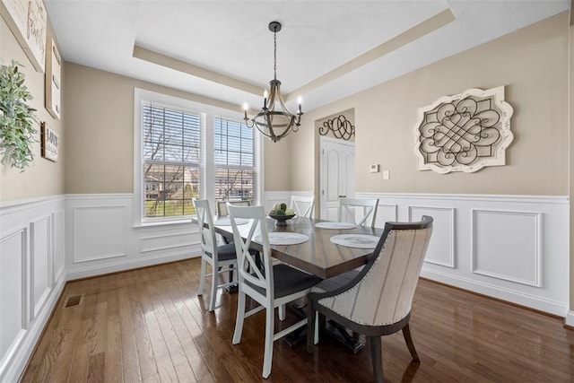 dining room featuring wainscoting, a decorative wall, dark wood-type flooring, a raised ceiling, and a notable chandelier