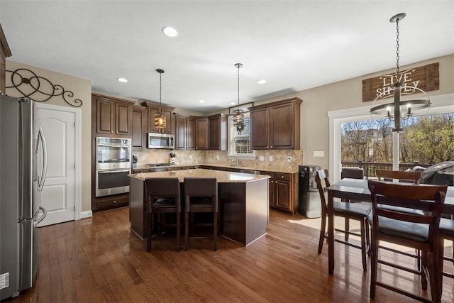 kitchen with appliances with stainless steel finishes, a chandelier, a center island, backsplash, and dark wood-style floors
