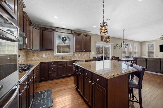 kitchen with appliances with stainless steel finishes, a breakfast bar, light wood finished floors, open floor plan, and a kitchen island