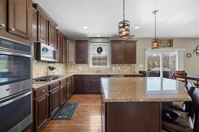 kitchen featuring a kitchen island, backsplash, light stone countertops, stainless steel appliances, and light wood-style flooring