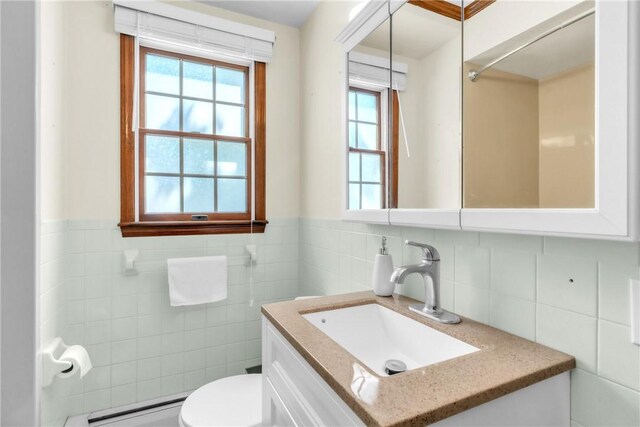 half bath featuring tile walls, plenty of natural light, baseboard heating, and toilet