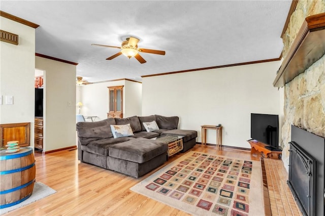 living area with crown molding, a glass covered fireplace, wood finished floors, baseboards, and ceiling fan