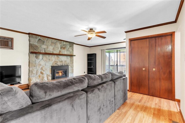 living room featuring light wood-style floors, ornamental molding, a stone fireplace, and ceiling fan