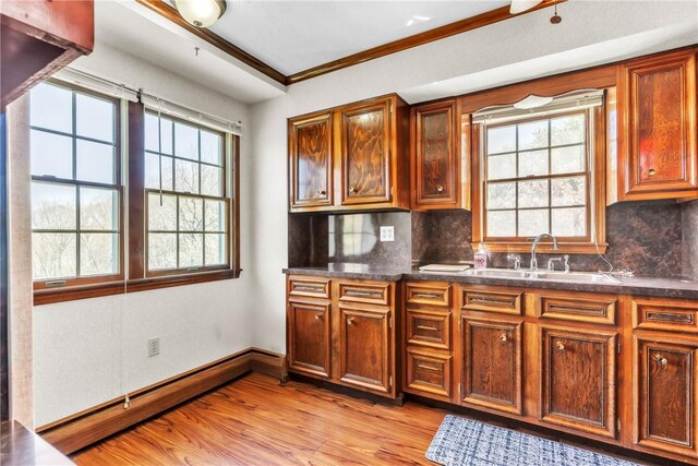 kitchen with a sink, light wood finished floors, dark countertops, and tasteful backsplash