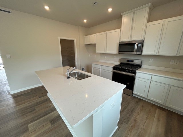 kitchen with dark wood-style floors, a center island with sink, white cabinetry, a sink, and stainless steel appliances