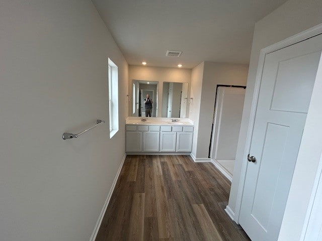 corridor featuring visible vents, a sink, baseboards, dark wood-style floors, and recessed lighting