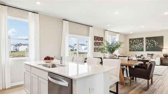 kitchen featuring stainless steel dishwasher, a center island with sink, a sink, light wood finished floors, and open floor plan