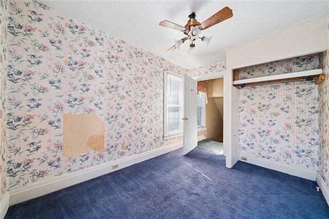 unfurnished bedroom featuring dark carpet, a ceiling fan, baseboards, and wallpapered walls