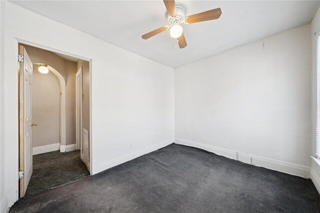 spare room with dark colored carpet, a ceiling fan, and baseboards
