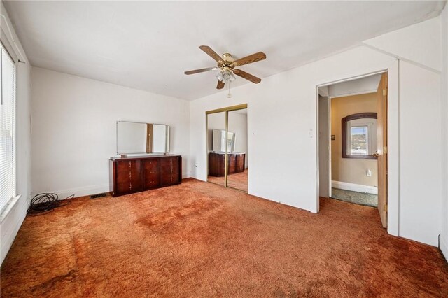 unfurnished bedroom featuring carpet flooring, a ceiling fan, multiple windows, and a closet