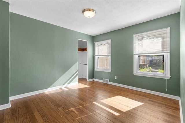 unfurnished room with wood-type flooring, baseboards, and visible vents