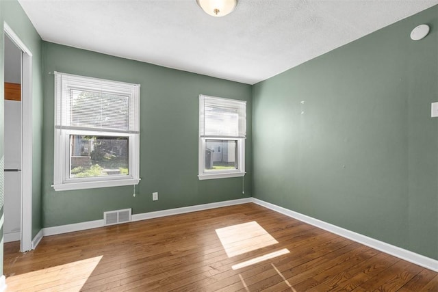 empty room featuring baseboards, hardwood / wood-style floors, and visible vents