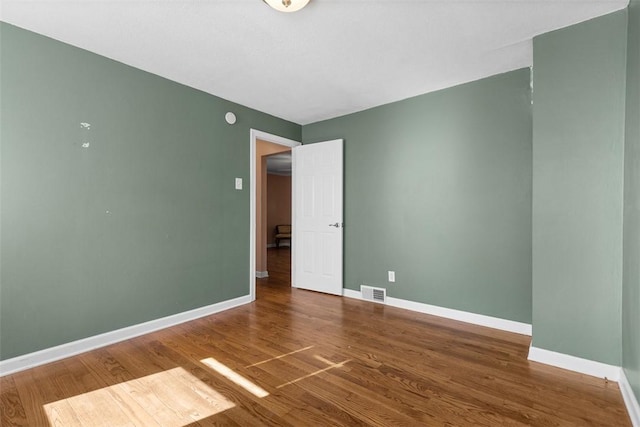 empty room with baseboards, wood finished floors, and visible vents