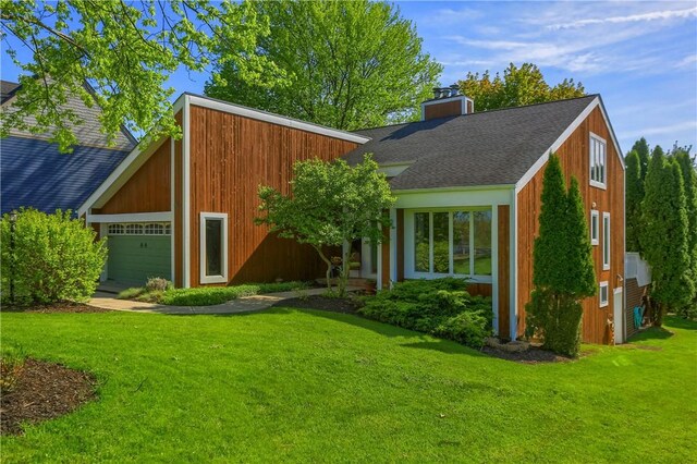 view of front of house featuring a garage, a chimney, roof with shingles, and a front yard