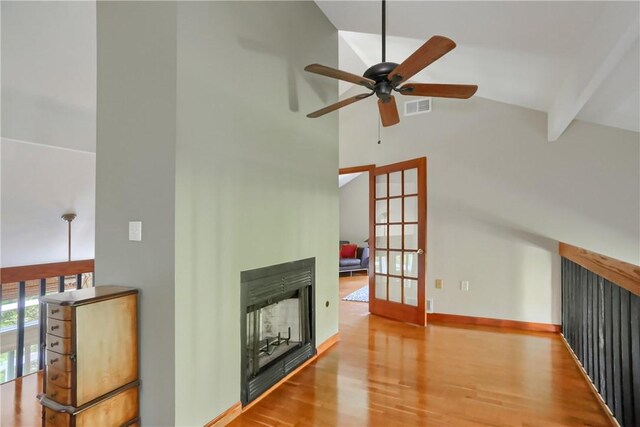 unfurnished living room featuring ceiling fan, high vaulted ceiling, a multi sided fireplace, wood finished floors, and visible vents