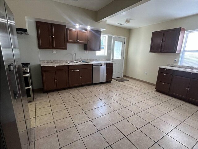 kitchen with dark brown cabinetry, appliances with stainless steel finishes, a sink, baseboards, and light tile patterned flooring