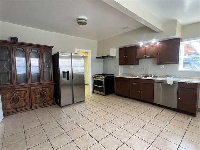 kitchen with a sink, light tile patterned flooring, dark brown cabinets, and stainless steel appliances