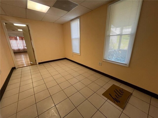 unfurnished room with light tile patterned flooring, baseboards, and a drop ceiling