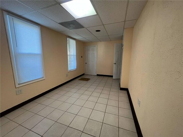 spare room with baseboards, a paneled ceiling, and light tile patterned floors