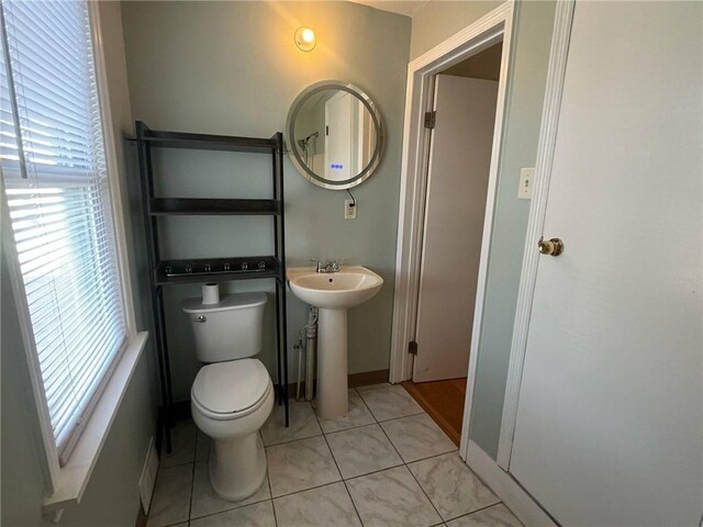half bathroom featuring baseboards, a sink, tile patterned floors, and toilet