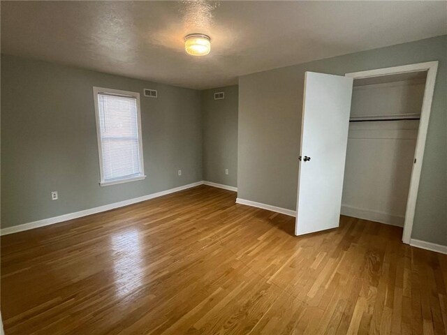 unfurnished bedroom with baseboards, wood finished floors, and visible vents