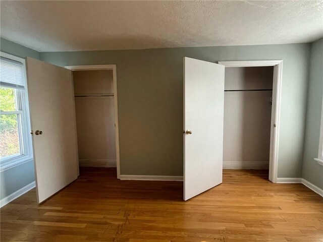unfurnished bedroom featuring baseboards, a textured ceiling, light wood finished floors, and a closet