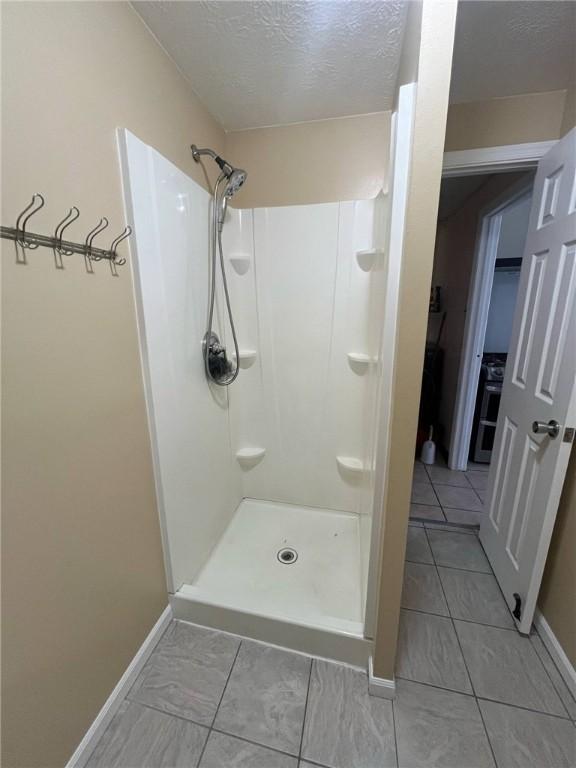 bathroom with baseboards, a textured ceiling, tile patterned floors, and a shower stall