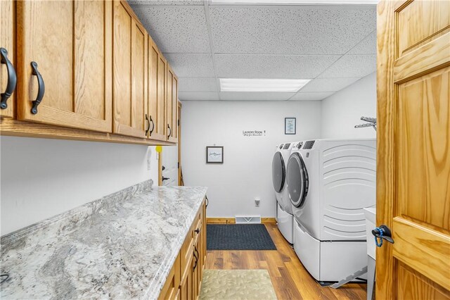 laundry room with cabinet space, separate washer and dryer, visible vents, and wood finished floors