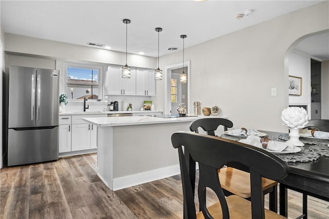 kitchen featuring arched walkways, wood finished floors, light countertops, white cabinets, and freestanding refrigerator