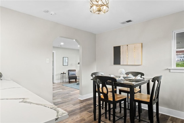 dining area featuring visible vents, arched walkways, baseboards, and wood finished floors