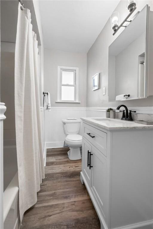 full bath featuring wainscoting, wood finished floors, vanity, toilet, and shower / bath combo with shower curtain