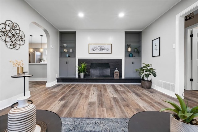 living room with visible vents, wood finished floors, baseboards, a fireplace with raised hearth, and arched walkways