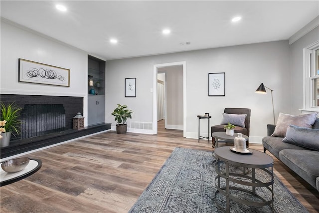 living room featuring baseboards, a fireplace, recessed lighting, and wood finished floors