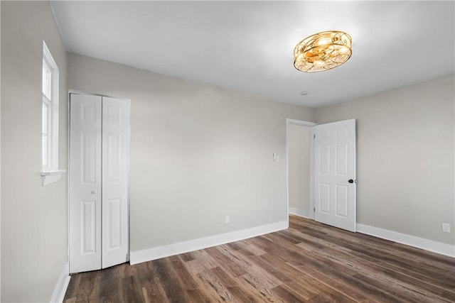 unfurnished bedroom with baseboards, dark wood-style floors, and a closet