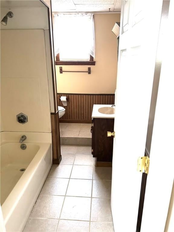 bathroom with wainscoting, tile patterned flooring, bathtub / shower combination, vanity, and toilet