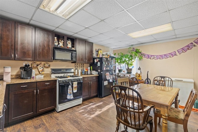 kitchen with dark brown cabinetry, dark wood finished floors, a drop ceiling, and black appliances