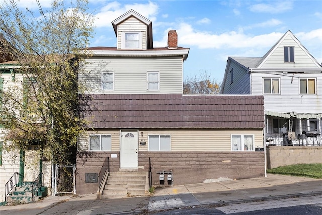 townhome / multi-family property featuring entry steps, fence, a chimney, and stone siding