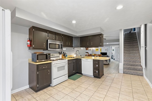 kitchen with a sink, white appliances, light countertops, a peninsula, and baseboards