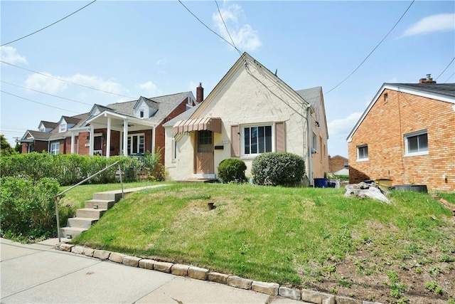view of front of home with a chimney, stucco siding, covered porch, and a front yard