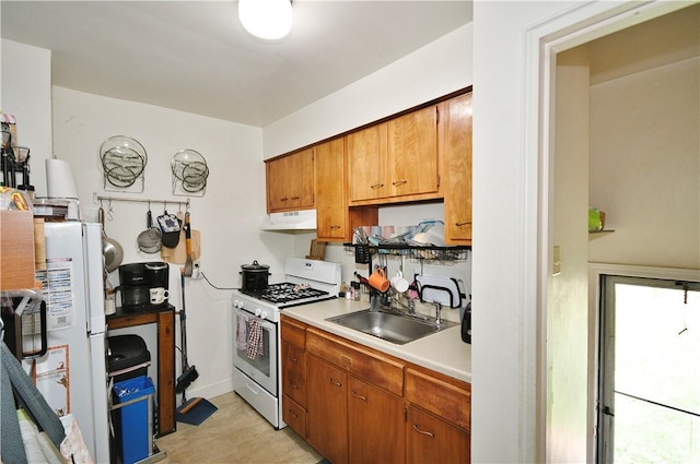 kitchen featuring white gas range oven, a sink, light countertops, baseboards, and under cabinet range hood