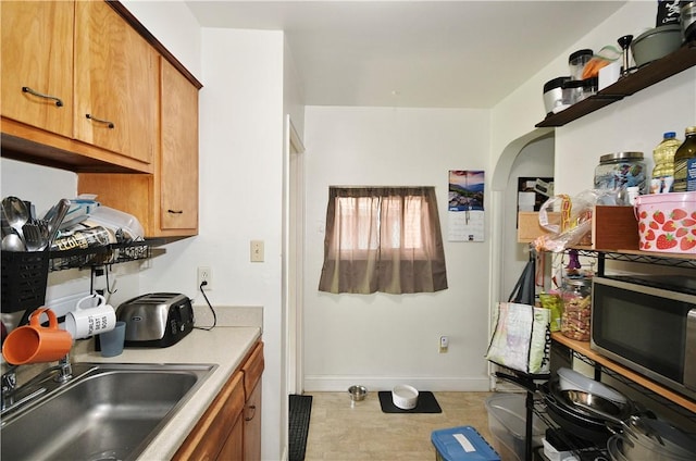 kitchen with a sink, light countertops, arched walkways, brown cabinetry, and baseboards