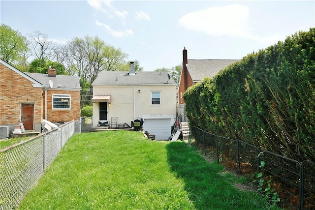back of property with an attached garage, a fenced backyard, a lawn, and central AC