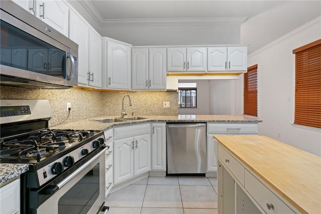 kitchen featuring a sink, ornamental molding, decorative backsplash, light tile patterned floors, and appliances with stainless steel finishes