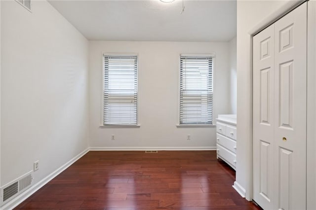 unfurnished bedroom with multiple windows, visible vents, and dark wood-style floors