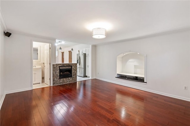 unfurnished living room featuring ornamental molding, hardwood / wood-style floors, a tiled fireplace, and baseboards