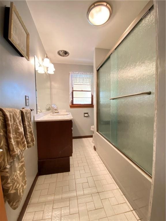 full bath featuring vanity, toilet, brick patterned floor, baseboards, and combined bath / shower with glass door