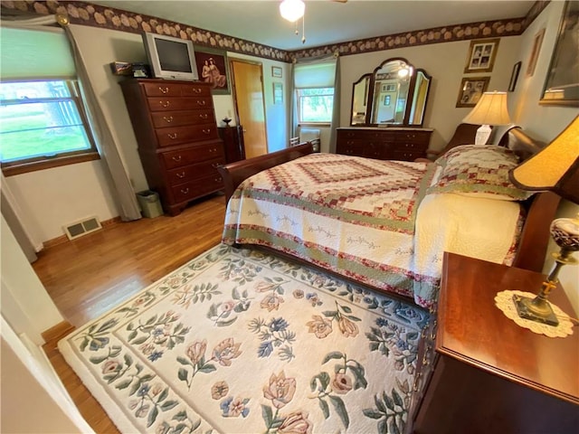 bedroom featuring visible vents, baseboards, wood finished floors, and multiple windows